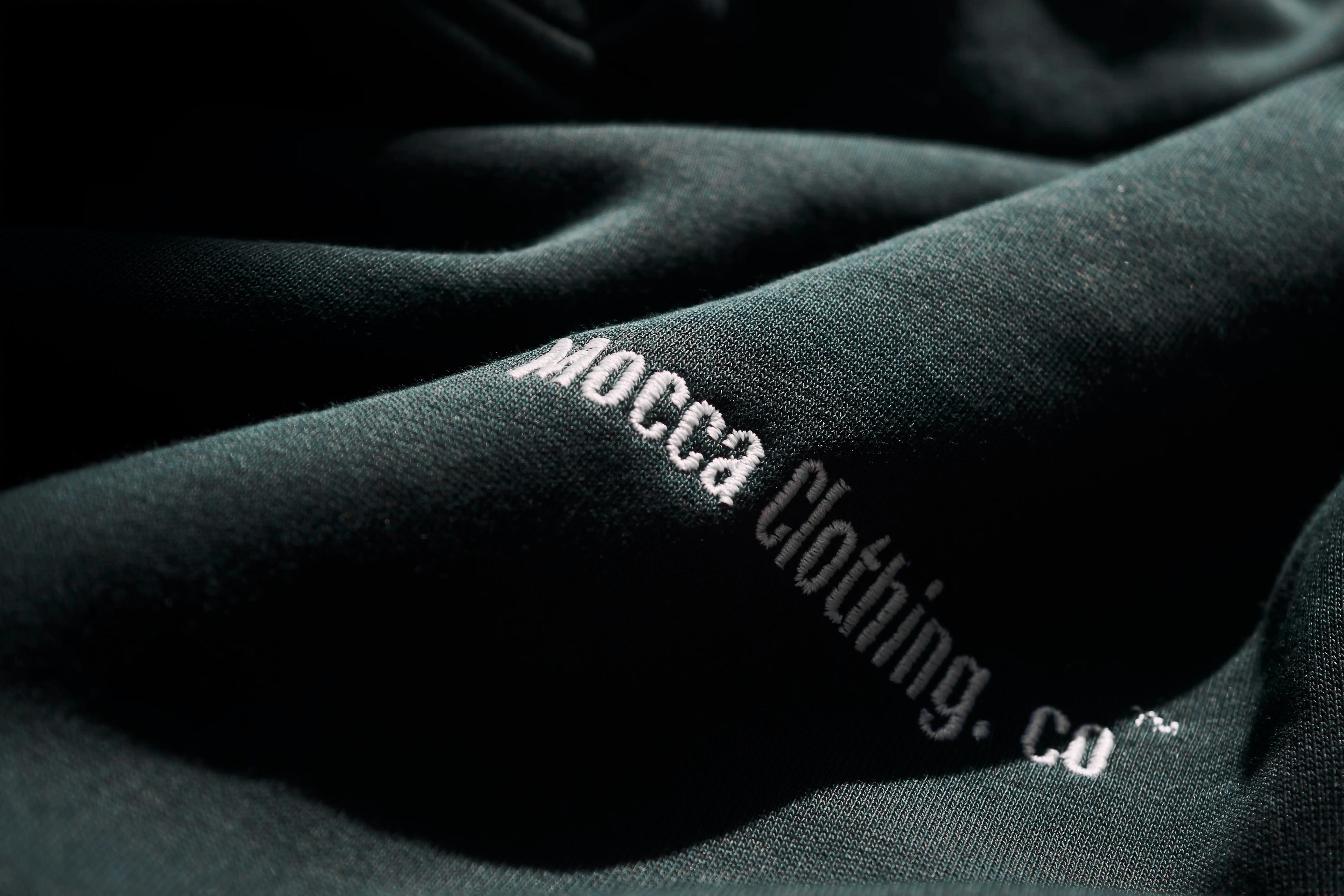 Close-up of a dark fabric with 'Mocca Clothing. Co' embroidered on it.
